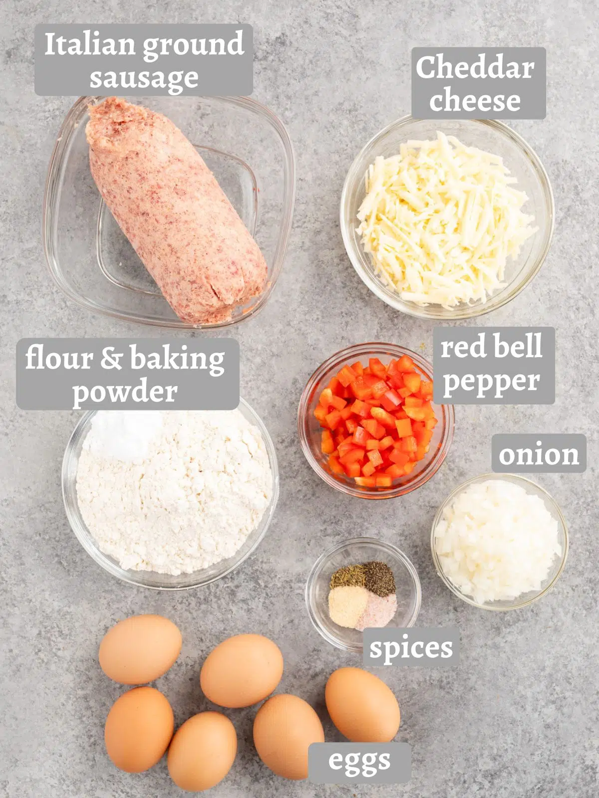 All ingredients for homemade sausage egg breakfast biscuits laid out: eggs, cheddar cheese, Italian sausage, bell pepper, onion, flour, baking powder, salt, pepper, garlic powder, and dried thyme.