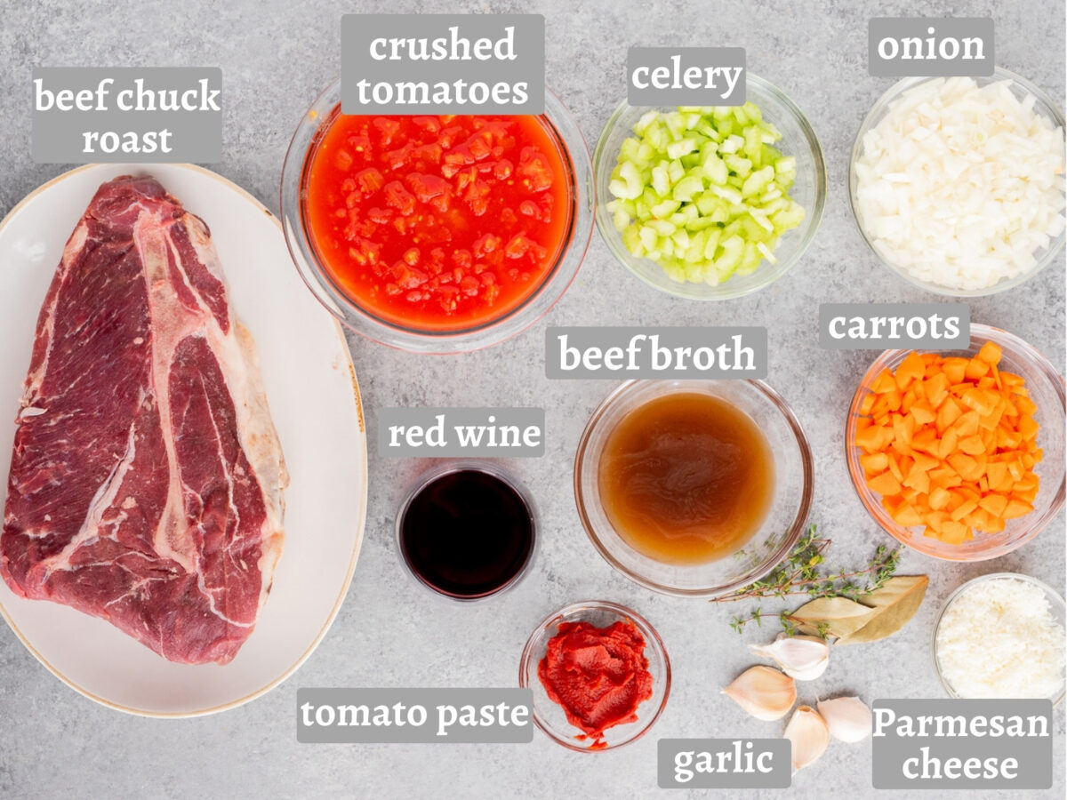 Ingredients for Slow Cooker Beef Ragu including beef chuck roast, crushed tomatoes, onion, celery, carrots, garlic, tomato paste, red wine, beef broth, thyme, bay leaves, and Parmesan cheese.