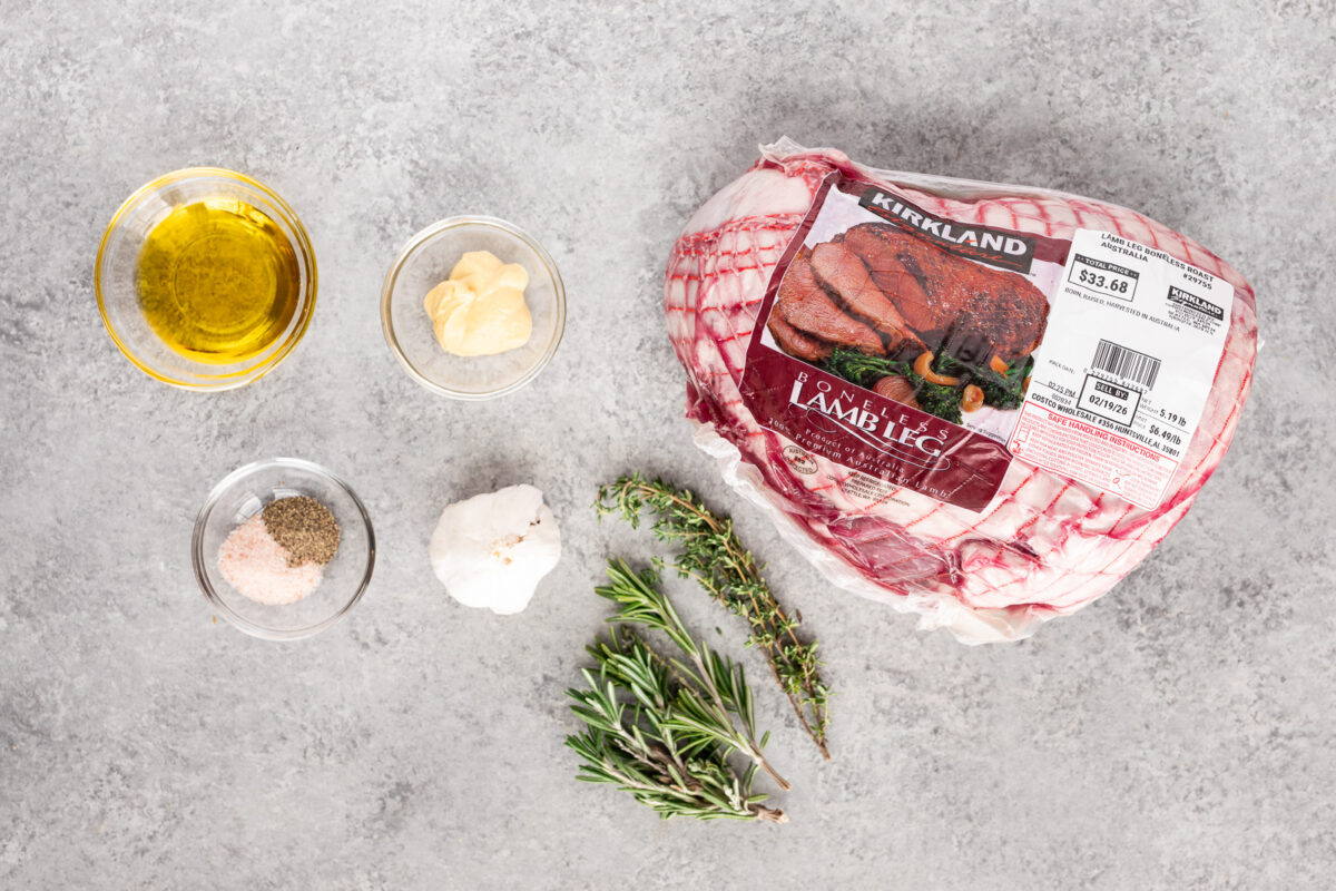 Ingredients for herb roasted leg of lamb including boneless lamb, garlic, rosemary, thyme, olive oil, salt, and pepper.