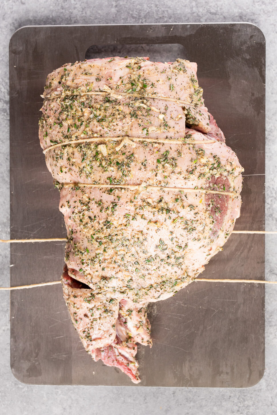Boneless leg of lamb tied with kitchen twine after being coated with herb garlic rub.
