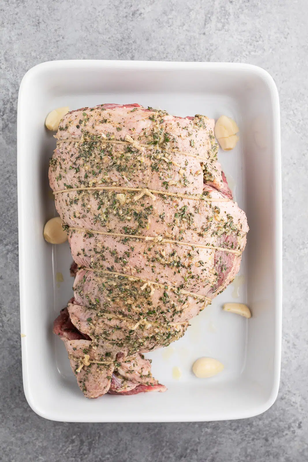 Herb-rubbed boneless leg of lamb placed in a roasting dish before cooking.