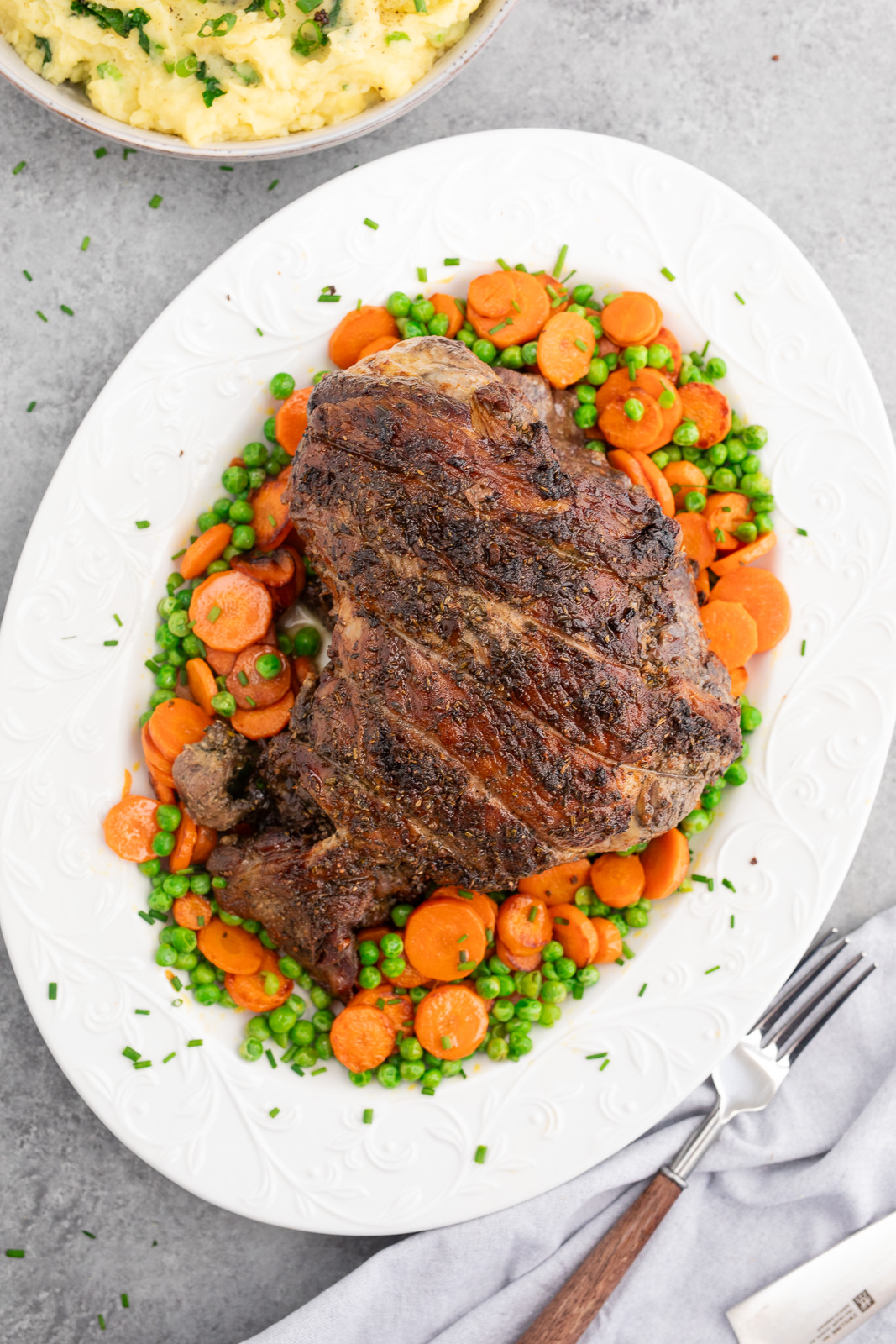 Herb roasted leg of lamb served with carrots and peas on a platter