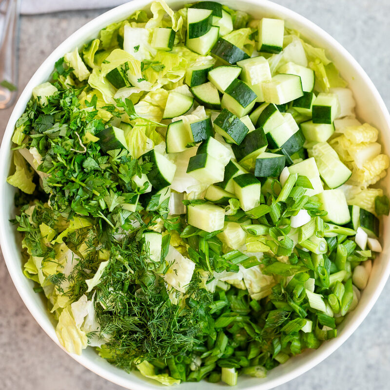 Thinly sliced romaine lettuce, cucumber & herbs in a large bowl for maroulosalata Greek lettuce salad