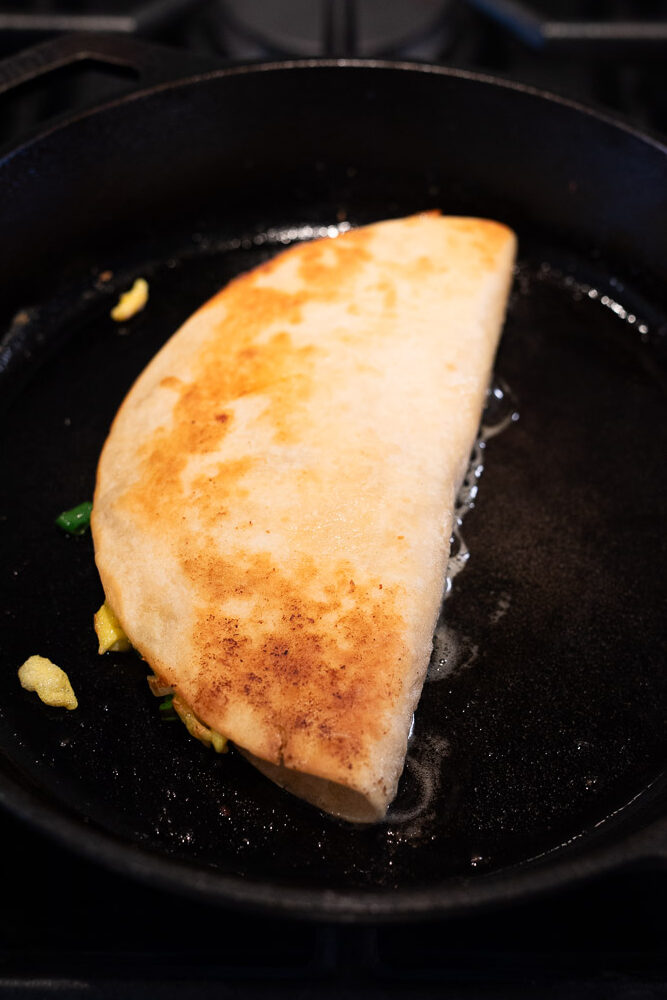 pan frying bacon and egg quesadilla in a skillet